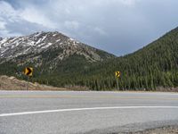 a mountain side with a road running next to the mountains, a bike parked in front of it and trees on one side