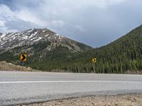 a mountain side with a road running next to the mountains, a bike parked in front of it and trees on one side