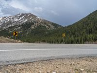 a mountain side with a road running next to the mountains, a bike parked in front of it and trees on one side