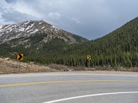 a mountain side with a road running next to the mountains, a bike parked in front of it and trees on one side