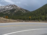 a mountain side with a road running next to the mountains, a bike parked in front of it and trees on one side