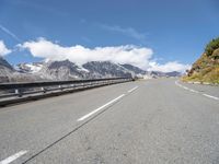 a long country road surrounded by snow capped mountains and rock sides with guard railing on both sides