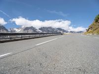 a long country road surrounded by snow capped mountains and rock sides with guard railing on both sides