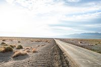 a country road in the middle of a barren field near mountains and a cloudy sky