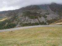 a car parked on a country road next to a tall mountain side with a low cloud above the top of it