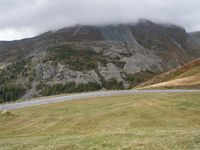 a car parked on a country road next to a tall mountain side with a low cloud above the top of it