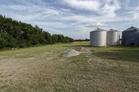 two large grain bins sit in the center of a field, surrounded by silos
