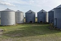 two large grain bins sit in the center of a field, surrounded by silos