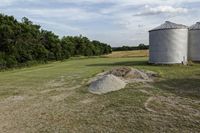 two large grain bins sit in the center of a field, surrounded by silos