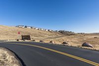 a curvy road going down the hill with houses behind it in the distance