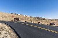 a curvy road going down the hill with houses behind it in the distance