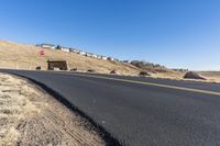 a curvy road going down the hill with houses behind it in the distance
