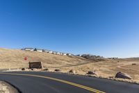 a curvy road going down the hill with houses behind it in the distance