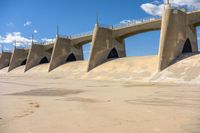 the dam wall with concrete walls and railings is covered in water with a blue sky