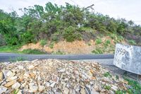 rocks are piled to be used as a road construction area along a highway, with an asphalt sign at the end