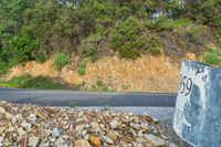 rocks are piled to be used as a road construction area along a highway, with an asphalt sign at the end