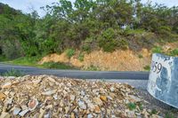 rocks are piled to be used as a road construction area along a highway, with an asphalt sign at the end