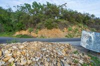 rocks are piled to be used as a road construction area along a highway, with an asphalt sign at the end