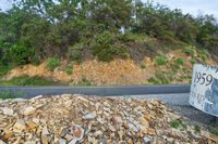 rocks are piled to be used as a road construction area along a highway, with an asphalt sign at the end