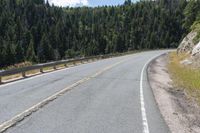 the asphalt road has some white marking on it and some trees, and a hill with hills