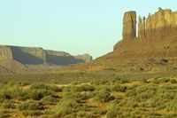 a horse standing in the desert with the mountains in the background, including large pillars and rocks