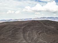 the desert is covered in thinly eroded layers and sand covered mountains and the clouds are still there