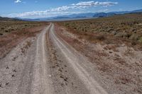 a dirt road winding through an empty field and mountain range in the distance to the right