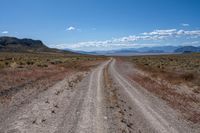 a dirt road winding through an empty field and mountain range in the distance to the right