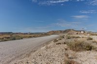 a lone road passing through a desert landscape with a house to the side and small buildings in the distance