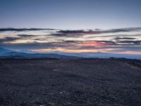 a barren field with mountains and red sky in the background near sunset on a cloudy day