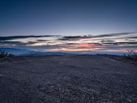 a barren field with mountains and red sky in the background near sunset on a cloudy day