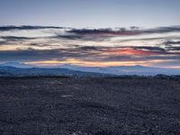 a barren field with mountains and red sky in the background near sunset on a cloudy day