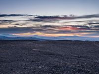 a barren field with mountains and red sky in the background near sunset on a cloudy day