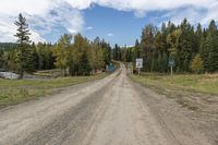 a dirt road leading to a wooden rail bridge with some colorful street signs above it