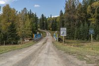 a dirt road leading to a wooden rail bridge with some colorful street signs above it