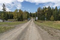 a dirt road leading to a wooden rail bridge with some colorful street signs above it