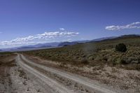 a dirt road leading to the mountains on a sunny day with white clouds and some blue sky