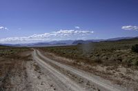 a dirt road leading to the mountains on a sunny day with white clouds and some blue sky