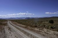 a dirt road leading to the mountains on a sunny day with white clouds and some blue sky