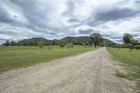 the dirt road leads up to the grassy area and towards a distant field with mountains behind it