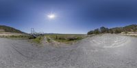 a 360 - angle picture of a dirt road near mountains and green grass with a bright sun in the distance