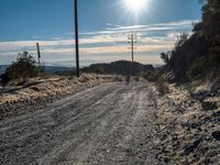 a dirt road through an empty mountain side with telephone poles next to it on a sunny day