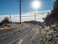 a dirt road through an empty mountain side with telephone poles next to it on a sunny day