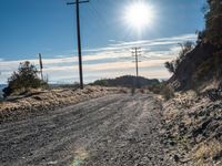 a dirt road through an empty mountain side with telephone poles next to it on a sunny day