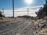 a dirt road through an empty mountain side with telephone poles next to it on a sunny day