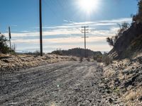 a dirt road through an empty mountain side with telephone poles next to it on a sunny day