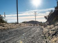 a dirt road through an empty mountain side with telephone poles next to it on a sunny day