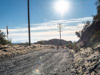 a dirt road through an empty mountain side with telephone poles next to it on a sunny day