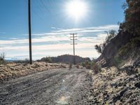 a dirt road through an empty mountain side with telephone poles next to it on a sunny day