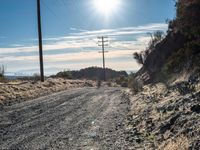 a dirt road through an empty mountain side with telephone poles next to it on a sunny day